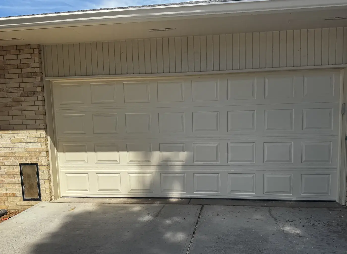 A newly installed 16 by 7 foot double garage door, almond raised-panel, on a brick house.