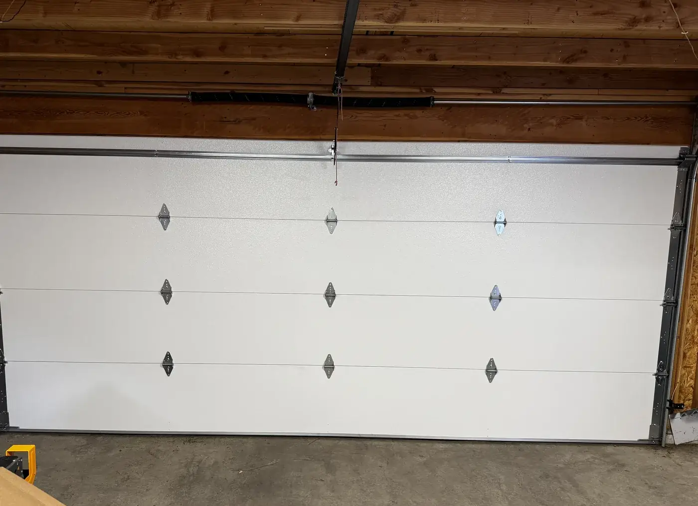 The inside of a newly installed insulated 16 by 7 foot garage door, almond, with a reinforcing strut and new tracks.