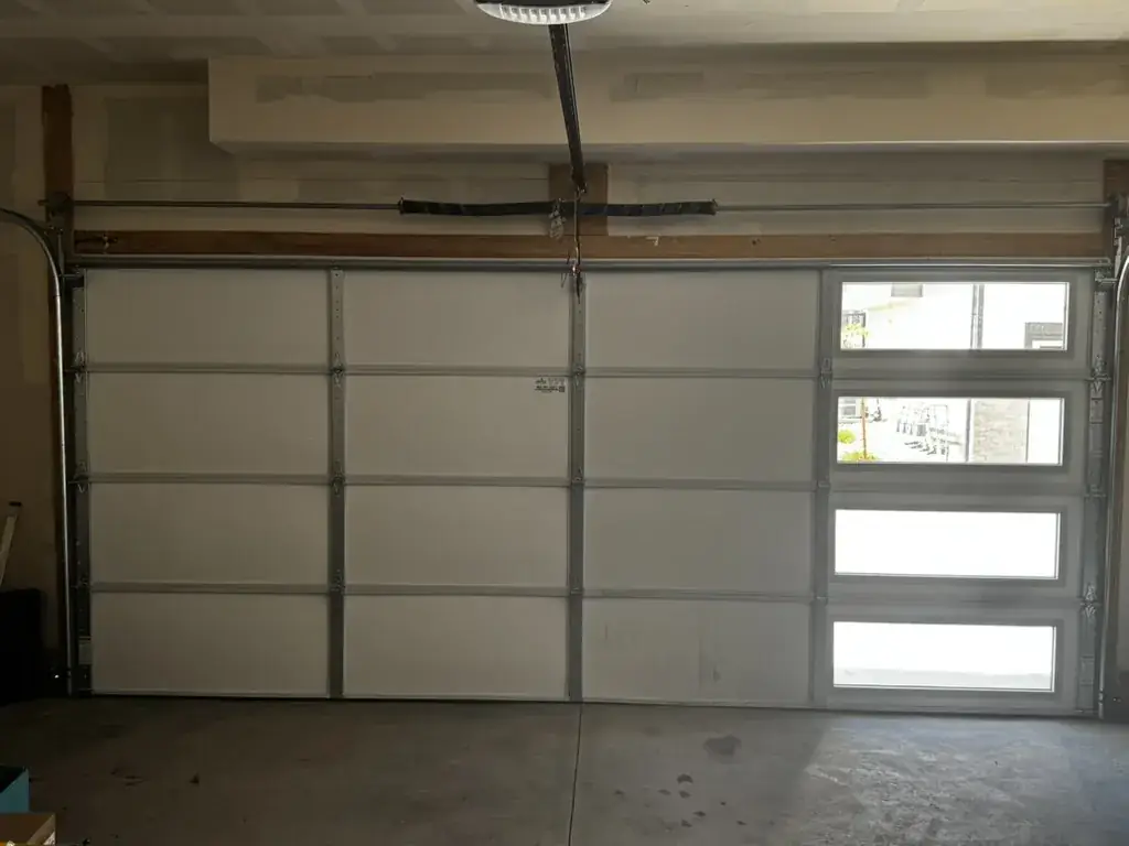 The inside of a white garage door with stacked windows on the right, torsion springs on the header.
