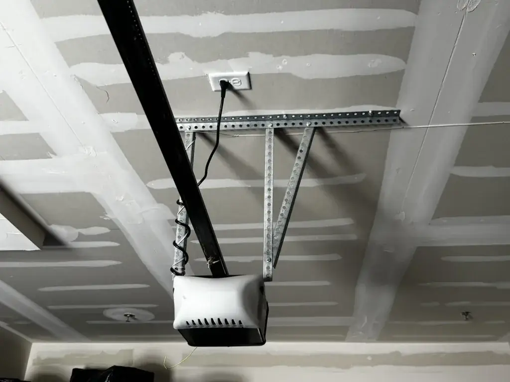 A white garage door opener hung from a steel ceiling bracket, black rail running to the header.