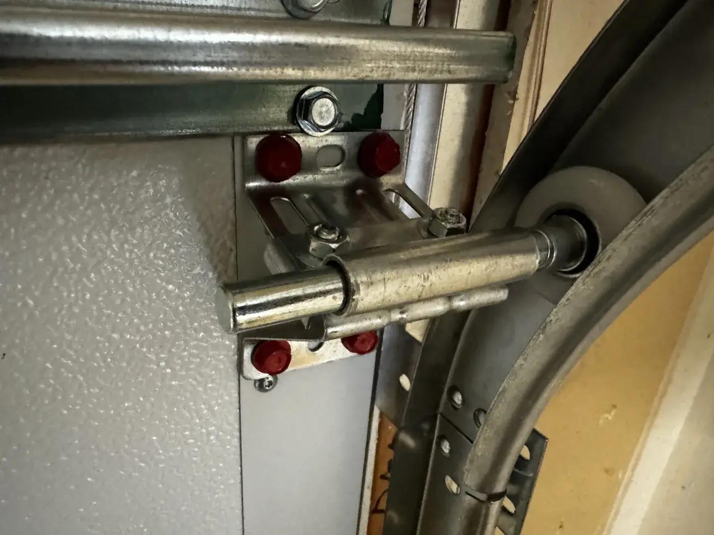 A roller and hinge bracket fixed to a garage door section at the track.