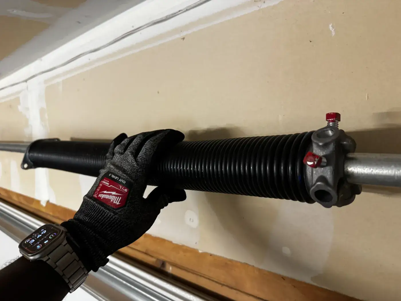 A gloved hand on a new torsion spring mounted on the shaft above a garage door.